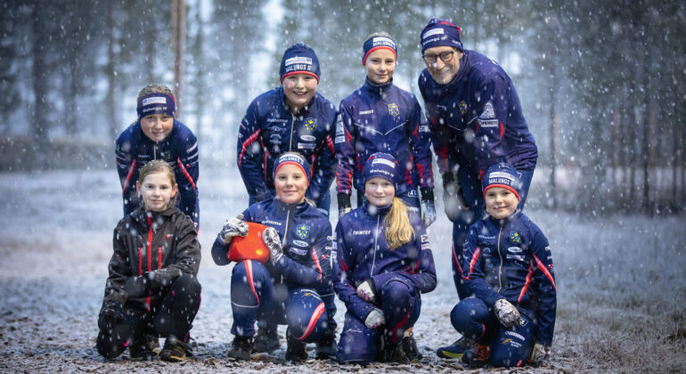 En gruppbild på Malungs IF - skidor. På bilden är det barn samt ledare som tittar in i kameran. Nysnö faller stämningsfullt.